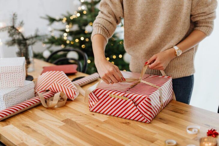 Woman Wrapping Gift near Christmas Tree